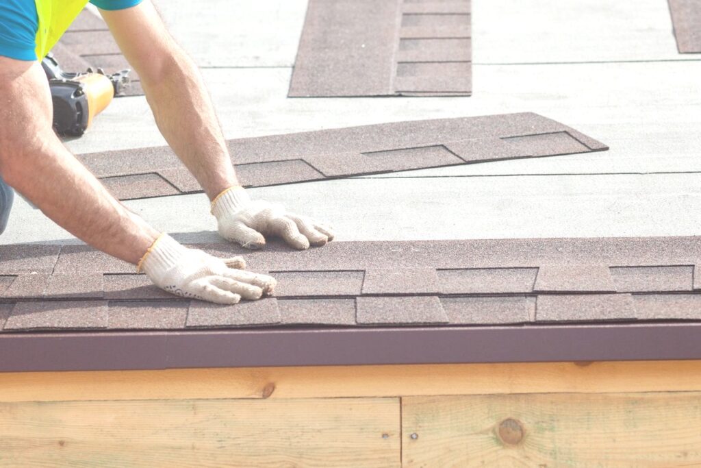 A person with gloves on standing over the roof of a house.